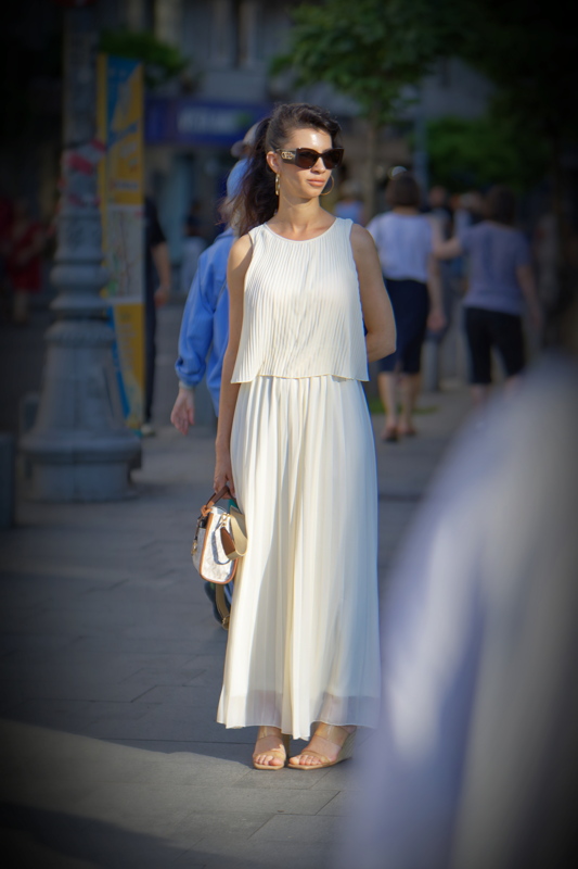 11 - Person wearing a white, sleeveless pleated dress featuring a draped bodice